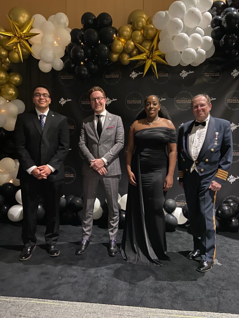 IMG_6825 Photo of Adam Gibson, Jeremy Diamond, John Wright, and Tonya Yearwood posing on gala backdrop with balloons.